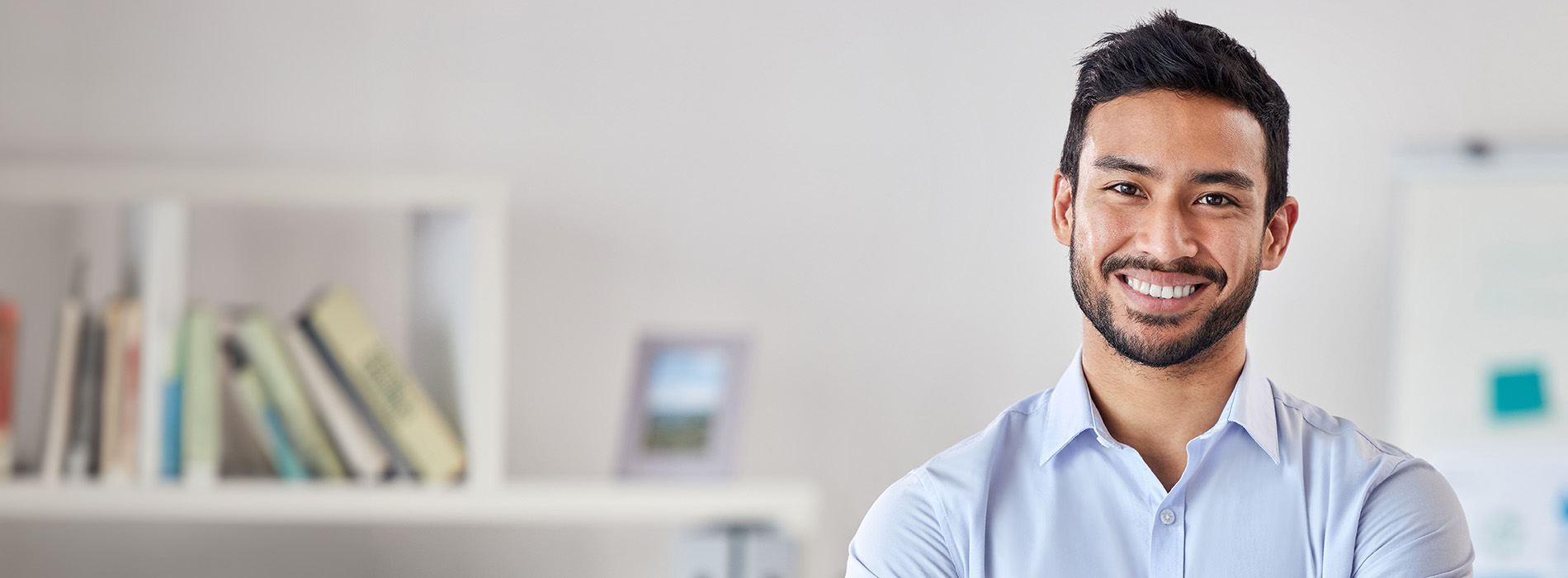 A smiling man stands confidently in front of bookshelves, suggesting an academic or professional setting.