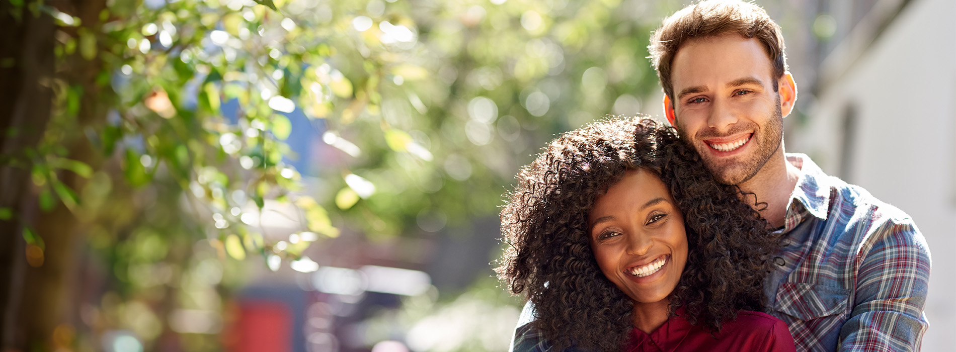 A young couple smiling at the camera, with the man on the left and the woman on the right, standing together outdoors during daylight.
